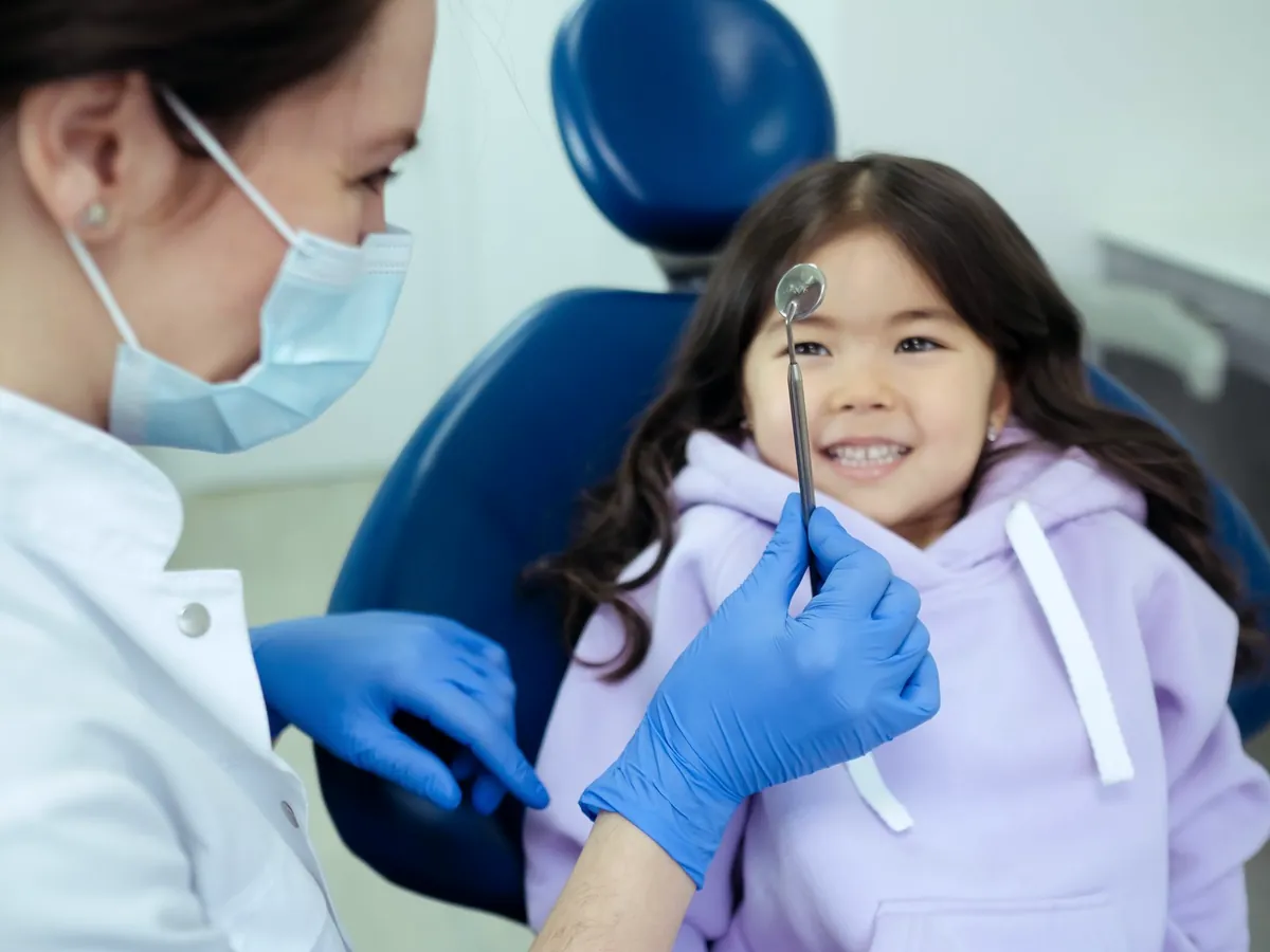 Young girl in a blue dental chair holding a dental mirror